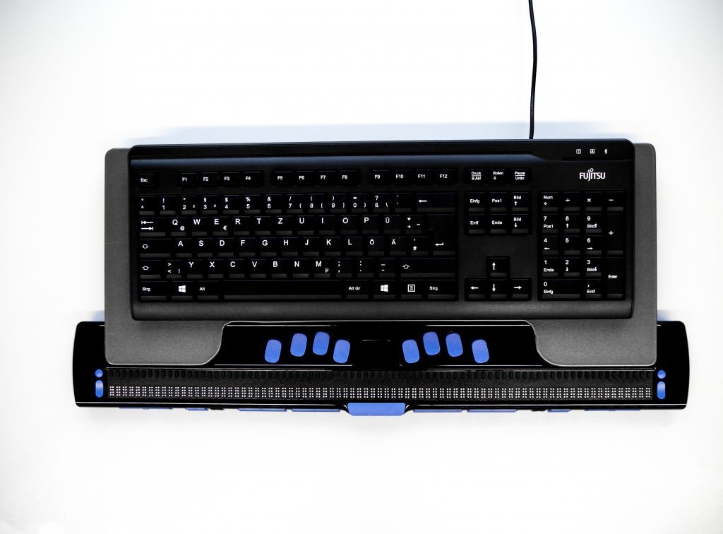 Bild zeigt die Braillezeile in Verwendung mit dem von uns eigens entworfenen Tastaturständer und einer Tastatur.